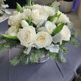 Low arrangement of white roses and tulips with pine branches in a gray pot