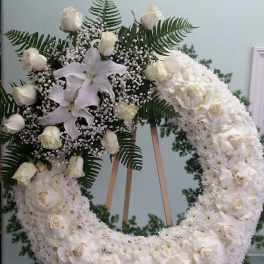 White floral wreath with roses, lilies, and fern accents on an easel