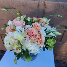Low arrangement of peach roses, white hydrangeas, and green orchids in a clear glass vase