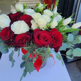 Low glass vase of red and white roses with white tulips and a red ribbon bow