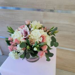 Low arrangement of pink roses, white hydrangeas, and lilies in a clear glass bowl vase