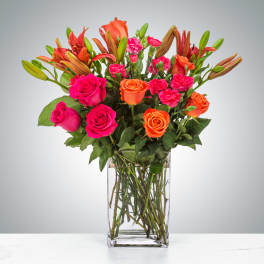 Bouquet of pink and orange roses with lilies in a clear glass vase