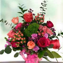 Mixed pink and red rose bouquet in a glass vase with a pink ribbon