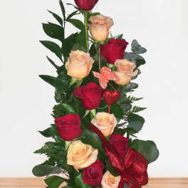 Tall arrangement of red and peach roses in a glass vase with ribbon and butterfly accents