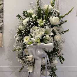 White funeral spray with lilies, roses, and a large ribbon on an easel