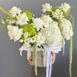 Large arrangement of white roses and hydrangeas with green accents in a silver hatbox container.