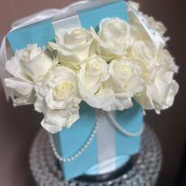 White roses arranged in a blue gift box with ribbon and pearl trim