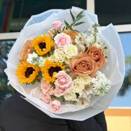 Bouquet of sunflowers, roses, and white flowers wrapped in white paper