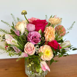 Mixed bouquet of pink, peach, and red flowers in a clear glass vase