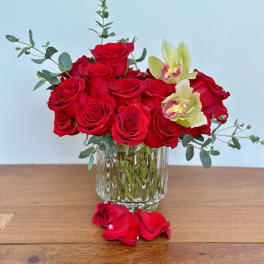 Red roses and pale orchids arranged in a clear glass vase