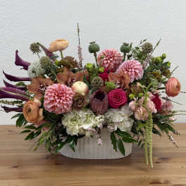 Low oval arrangement of pink dahlias, roses, calla lilies and mixed blooms in a white ceramic vase.