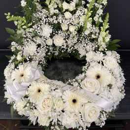 White floral funeral wreath with roses, daisies, and ribbon
