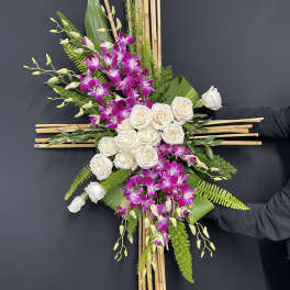 Cross-shaped floral arrangement with white roses and purple orchids on bamboo