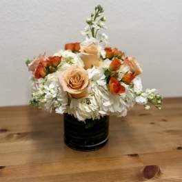 Peach roses and white flowers arranged in a black vase