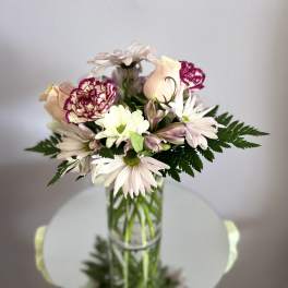 Mixed bouquet of pale daisies, carnations, and roses in a glass vase