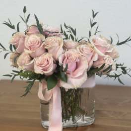 Pink roses arranged in a clear glass vase with a pink ribbon