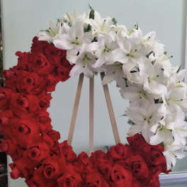 Heart-shaped wreath of red roses and white lilies on a wooden stand