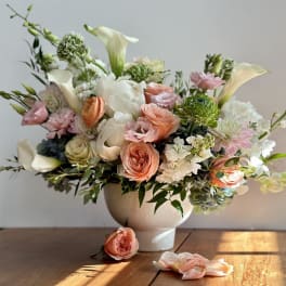 Pastel floral arrangement in a white vase with roses and calla lilies