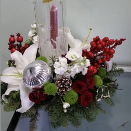 Holiday floral centerpiece with white lilies, red roses, and a tall red candle