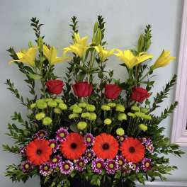 Tall mixed flower arrangement with yellow lilies, red roses, and bright daisies