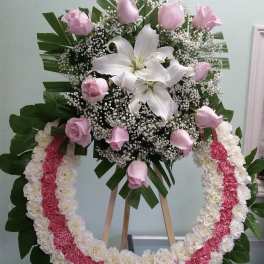 Pink roses and white lilies in a standing floral wreath with a pink-and-white garland