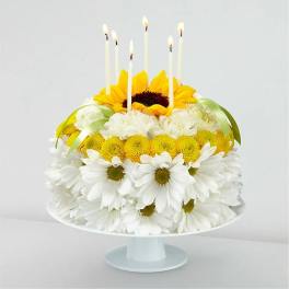 Flower cake with white daisies and yellow blooms topped by lit candles