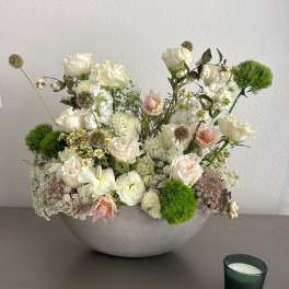 White floral arrangement in a gray bowl with a small candle beside it