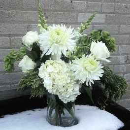 White floral arrangement in a clear glass vase with green accents