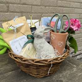 Gift basket with potted pink flowers, herb packets, gloves, and garden tools