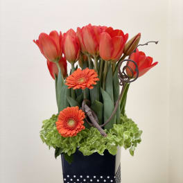 Red tulips and orange gerbera daisies in a tall black vase