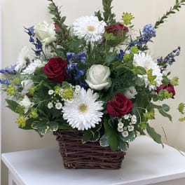 Basket arrangement with red and white roses, white daisies, and blue flowers