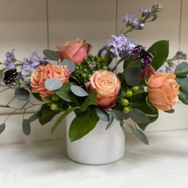Peach roses and lavender flowers in a white vase