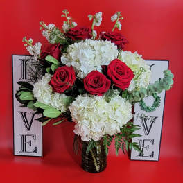 Red roses and white hydrangeas in a glass vase with decorative letters behind