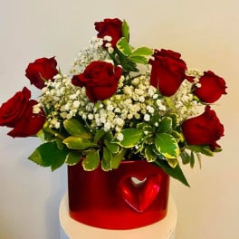Red roses arranged in a red heart vase with white filler flowers