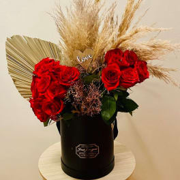 Red roses in a black hatbox with dried pampas grass and a small heart topper