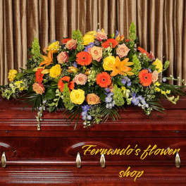 Bright orange and yellow casket spray with roses, gerbera daisies, and lilies on a wooden casket
