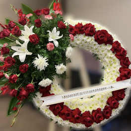 Standing wreath of red roses and white flowers with a side spray on a white ribbon banner.