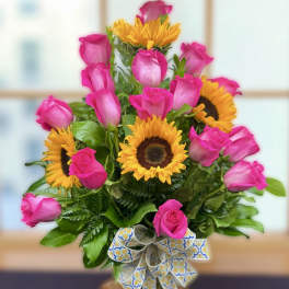 Arrangement of bright pink roses and yellow sunflowers in a glass vase with a patterned ribbon bow