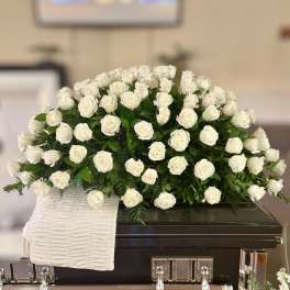 White rose casket spray on a dark casket with a white cloth drape