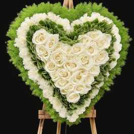 Heart-shaped floral wreath with white roses and green ruffled flowers on an easel