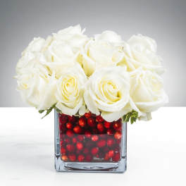 Compact arrangement of white roses in a square glass vase filled with red berries