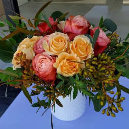 Peach and pink rose arrangement with berries in a white ceramic vase