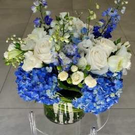 Low arrangement of white roses and blue hydrangeas in a clear glass vase.
