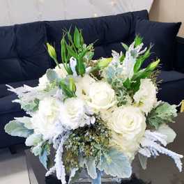 Low white rose and lisianthus arrangement in a clear glass cube vase.