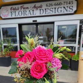 Compact arrangement of bright pink roses and mixed blooms in a small decorative vase, held outside a flower shop.