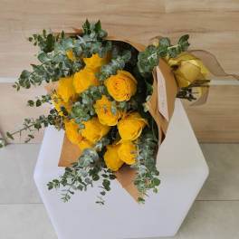 Wrapped bouquet of bright yellow roses and eucalyptus laid on a white stand
