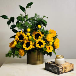 Sunflower arrangement in a gold vase with green foliage