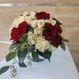 Low round arrangement of red and cream roses with hydrangeas in a clear glass bowl vase