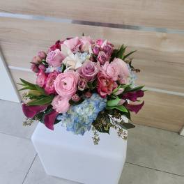Rounded bouquet of pink roses, ranunculus, lilies and blue hydrangeas in a compact arrangement.