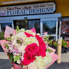Hand-tied bouquet of hot pink and white roses with white hydrangeas and pastel blooms in pink wrap.